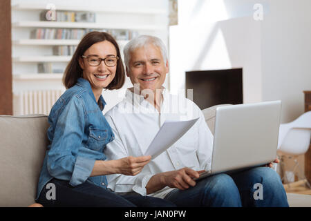 Couple à l'aide de leur ordinateur portable pour payer leurs factures à la maison dans le salon Banque D'Images