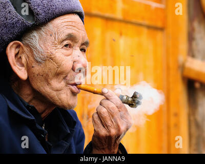 ZHAOXING, CHINE - 11 NOVEMBRE 2010 : Old Chinese reposant sur la porte de son chalet fumant une pipe dans le village Zhaoxing Banque D'Images