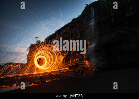 Cercles de lumière créé par la lumière peinture avec burning laine métallique dans un endroit magnifique sur une plage de Bali avec une chute d'une falaise s'écrouler Banque D'Images