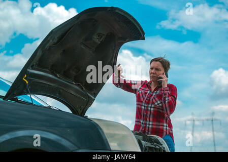 Des profils caucasian woman standing par la rupture de la voiture sur route de campagne et talking on mobile phone Banque D'Images