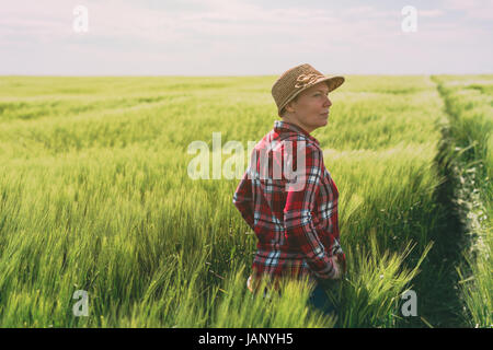 Concept de l'agriculture responsable, la productrice en cultures de céréales, agronome à la femme de terrain sur le champ de blé à l'horizon par un jour de vent et p Banque D'Images