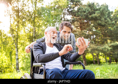 Père et fils Hipster en fauteuil roulant à la prise du parc. selfies Banque D'Images