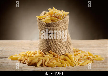 Sac en jute avec variété de pâtes alimentaires non cuites sur table en bois Banque D'Images