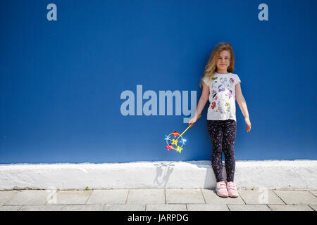 Six ans de l'école heureuse fille blonde debout près du mur bleu d'été, piscine. Banque D'Images