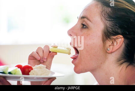 Jeune femme dans la vingtaine, consommer des aliments sains de concombre avec humous hoummos ou hommous fait à partir de pois chiches cuits, d'épices l'ail, le tahini, l'huile d'olive et Banque D'Images