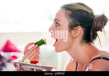 Jeune femme dans la vingtaine, consommer des aliments sains de concombre avec humous hoummos ou hommous fait à partir de pois chiches cuits, d'épices l'ail, le tahini, l'huile d'olive et Banque D'Images