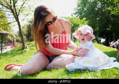 Jeune mère dans la vingtaine avec ses six mois baby girl wearing sun hat et s'habiller dans un parc Banque D'Images