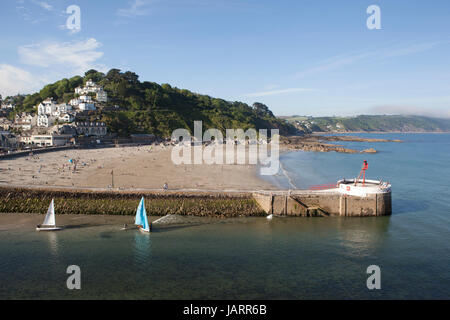 Petits dériveurs avec voiles multicolores partir en mer à Looe, Cornwall. Le banjo pier et plage sont au premier plan et la ville est vue sur la colline. Banque D'Images