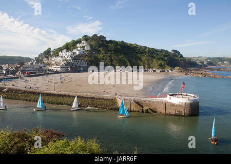 Petits dériveurs avec voiles multicolores partir en mer à Looe, Cornwall. Le banjo pier et plage sont au premier plan et la ville est vue sur la colline. Banque D'Images