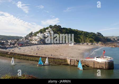 Petits dériveurs avec voiles multicolores partir en mer à Looe, Cornwall. Le banjo pier et plage sont au premier plan et la ville est vue sur la colline. Banque D'Images