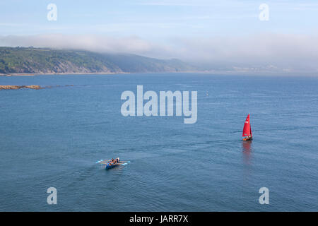 Sea mist rolls dans à la côte à Looe, Cornwall comme un canot et un rouge navigué concert pilotes font leur chemin vers la mer. Banque D'Images