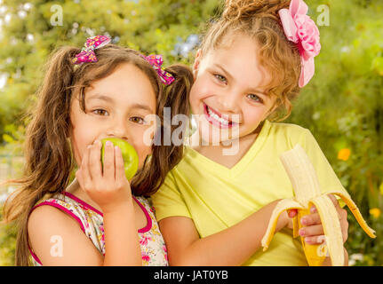 Deux belles jeunes filles, manger une pomme et banane sain dans un jardin historique. Banque D'Images