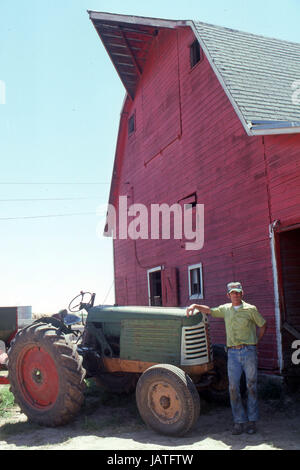 Agriculteur dans le Nebraska avec un vieux tracteur devant une grande grange rouge Banque D'Images