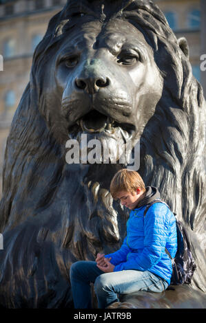 Londres - le 31 octobre 2016 : les jeunes'pose devant l'un des quatre lions en bronze au pied de la Colonne Nelson à Trafalgar Square. Banque D'Images