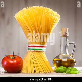 Paquet de spaghetti à l'Italienne non cuites attaché avec un ruban aux couleurs du drapeau national - rouge, blanc et vert - sur un comptoir de cuisine avec des feuilles de basilic frais, tomate et un pot d'huile d'olive Banque D'Images