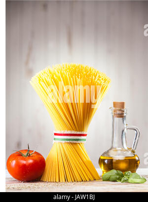 Spaghetti à l'Italienne non cuites attaché avec un ruban aux couleurs du drapeau national - rouge, blanc et vert, debout sur un comptoir de cuisine avec tomate et basilic frais et un pot d'huile d'olive Banque D'Images