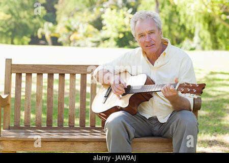 L'homme se tourne vers l'avenir tout en jouant une guitare comme il est assis sur un banc Banque D'Images