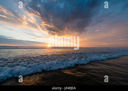 Sous une tempête/une marée montante vagues pousse sur une plage au coucher du soleil. Banque D'Images