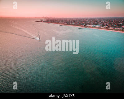 Vue aérienne de bateau à voile à travers la baie Port Phillip avec littoral et les banlieues de Melbourne dans l'arrière-plan dans le magnifique coucher du soleil Banque D'Images