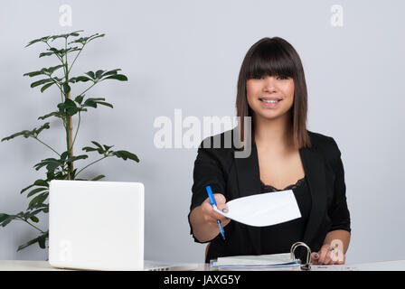 Junge Frau sitzt am Schreibtisch und überreicht ein Blatt Papier Banque D'Images