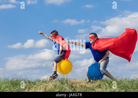 Père et fils jouer au super-héros de la journée. Les gens s'amuser en plein air.Ils sauter sur des ballons gonflables sur la pelouse. Concept de famille accueillante. Banque D'Images