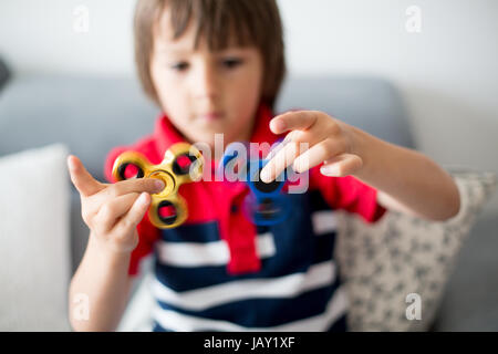 Petit enfant, garçon, jouant avec deux fidget spinner toys pour soulager le stress à la maison Banque D'Images