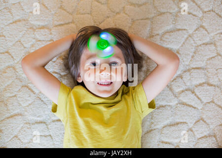 Petit enfant, garçon, jouant avec lumineux vert fidget spinner toy pour soulager le stress à la maison Banque D'Images