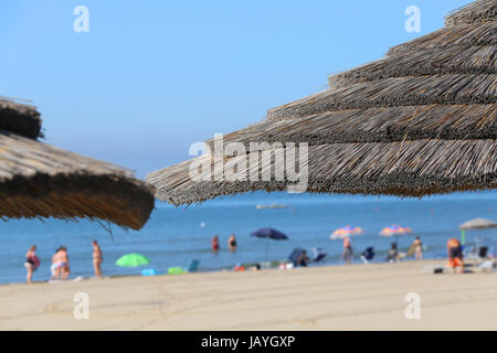 Grand parasol de paille à l'abri du chaud soleil d'été au bord de la mer avec de nombreuses personnes dans l'océan Banque D'Images