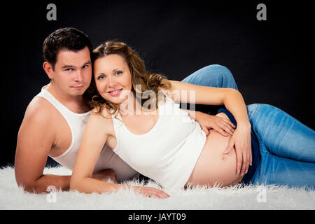 La grossesse couple lying hugging sur fond noir Banque D'Images
