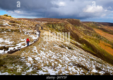 Une femelle Walker sur le chemin le long de la limite sud de Kinder scout dans le parc national de Peak District., avec la lumière de la neige au sol Banque D'Images