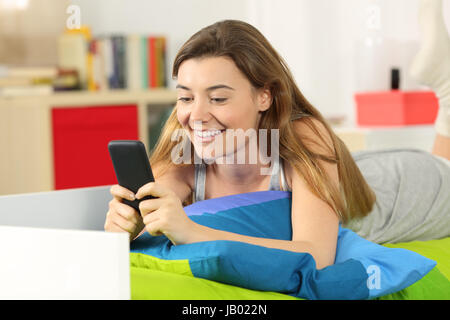 Seule la lecture des messages de l'adolescence sur le téléphone mobile étendu sur le lit dans sa chambre Banque D'Images