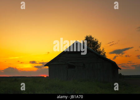 Une vieille grange maison se trouve sur le début de l'été, champs de la Finlande du Nord. Le soleil se couche très tard dans la soirée. Banque D'Images