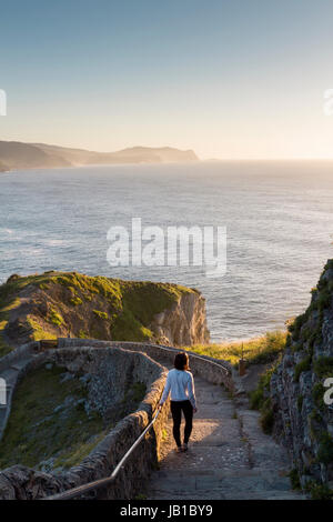 Une jeune femme descendant l'escalier de pierre surplombant la côte à San Juan de Gaztelugatxe, pays Basque, pendant l'heure dorée Banque D'Images