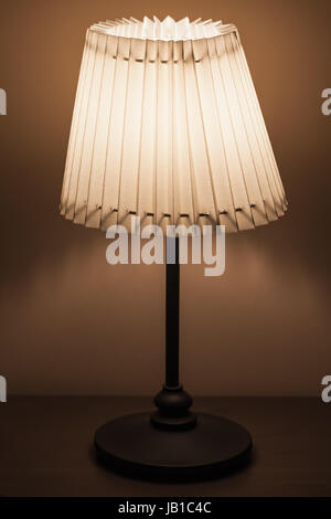 Lampe classique avec abat-jour en tissu ronde se tient près du mur dans une pièce sombre Banque D'Images
