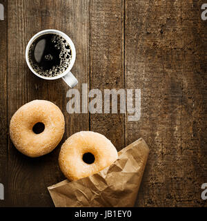 Close up Vue de dessus de deux délicieux donut bague sucrées avec une machine à expresso et de paquets de papier brun froissé sur une surface en bois rustique avec copyspace pour un séjour détente pause café Banque D'Images
