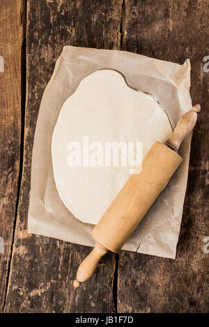 Vue aérienne de fraîchement mis en œuvre et de la pâte d'un rouleau à pâtisserie en bois rétro durant la préparation de la base ou de pâte à tarte pour une pizza italienne sur une feuille de papier sulfurisé sur une table en bois rustique Banque D'Images