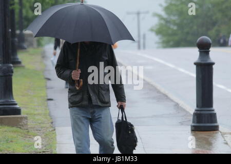 Homme portant un manteau noir couvrant la tête avec un parapluie Banque D'Images