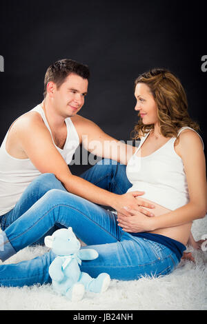 La grossesse couple lying hugging sur fond noir Banque D'Images