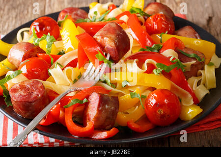 Pâtes fettuccine avec poivre, tomates saucisses frites et gros plan sur une plaque horizontale. Banque D'Images