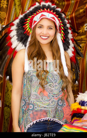 Une belle jeune femme portant Native American hat plume. avec des tissus de couleurs arrière-plan. Banque D'Images