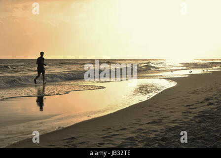 Homme qui court à travers les vagues vers le soleil aveuglant Banque D'Images