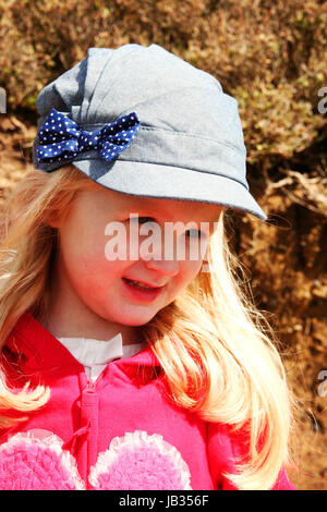 Photo d'une fille de trois ans aux cheveux longs blonds et chapeau en denim avec un noeud sur lui au soleil petite fille blonde Banque D'Images