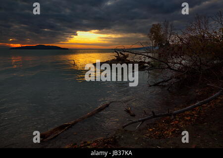 Un très sombre et moody photo d'un coucher de soleil sur le lac, avec des arbres et des plantes dans l'ombre et de la lumière du soleil forte d'être sorti d'un trou dans les nuages Banque D'Images