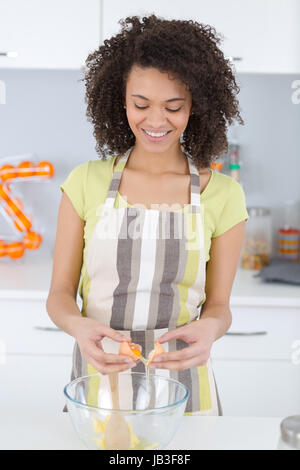 Jeune femme casser un oeuf pour faire la pâte à biscuits Banque D'Images