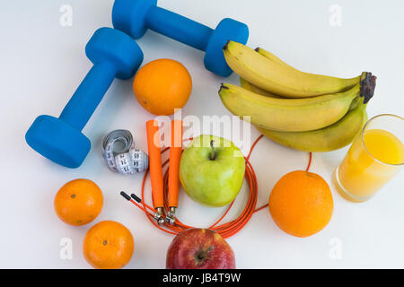 Concept de saine alimentation. Corde à sauter, haltères, bananes, oranges, ruban à mesurer la taille, des oranges, pomme rouge, pomme verte, jus d'orange sur un onglet blanc Banque D'Images