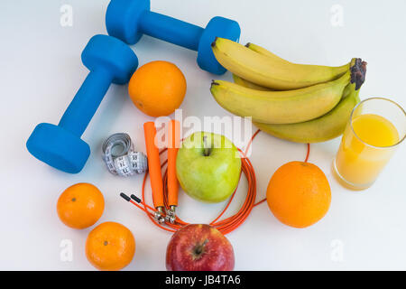 Concept de saine alimentation. Corde à sauter, haltères, bananes, oranges, ruban à mesurer la taille, des oranges, pomme rouge, pomme verte, jus d'orange sur un onglet blanc Banque D'Images