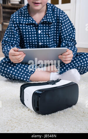 Garçon avec casque de réalité virtuelle et tablette numérique assis sur tapis à Accueil Banque D'Images