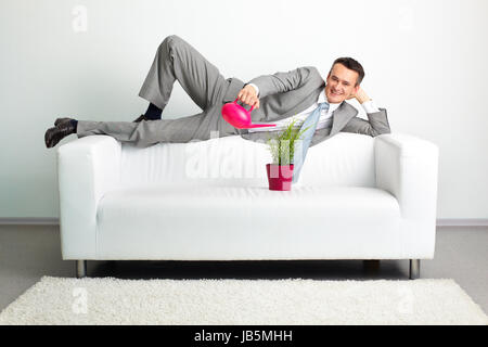 Photo de l'homme heureux d'arroser plante tout en lying on sofa Banque D'Images