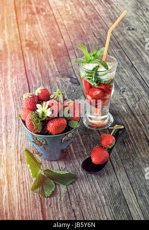 Les fraises dans un bol en céramique sur la vitre de l'arrière-plan avec une fraise verre sur table en bois sur une journée ensoleillée. Banque D'Images