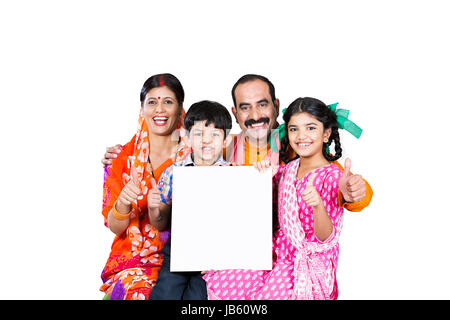 Heureux de la famille rurale indienne- parents avec 2 enfants assis ensemble Showing Thumbs up avec tableau blanc sur fond blanc Banque D'Images